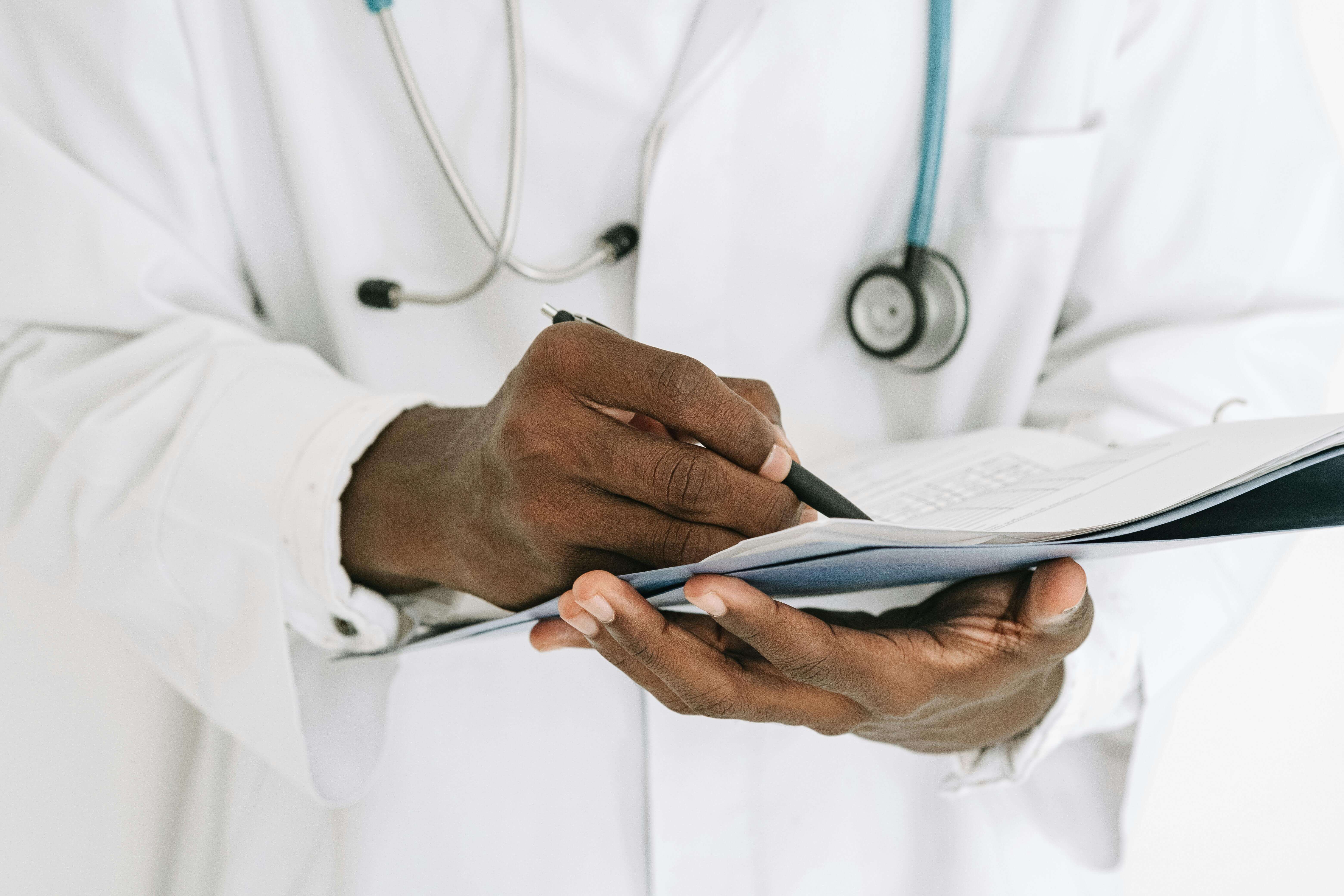 Doctor's hands holding a notepad and pen taking notes.